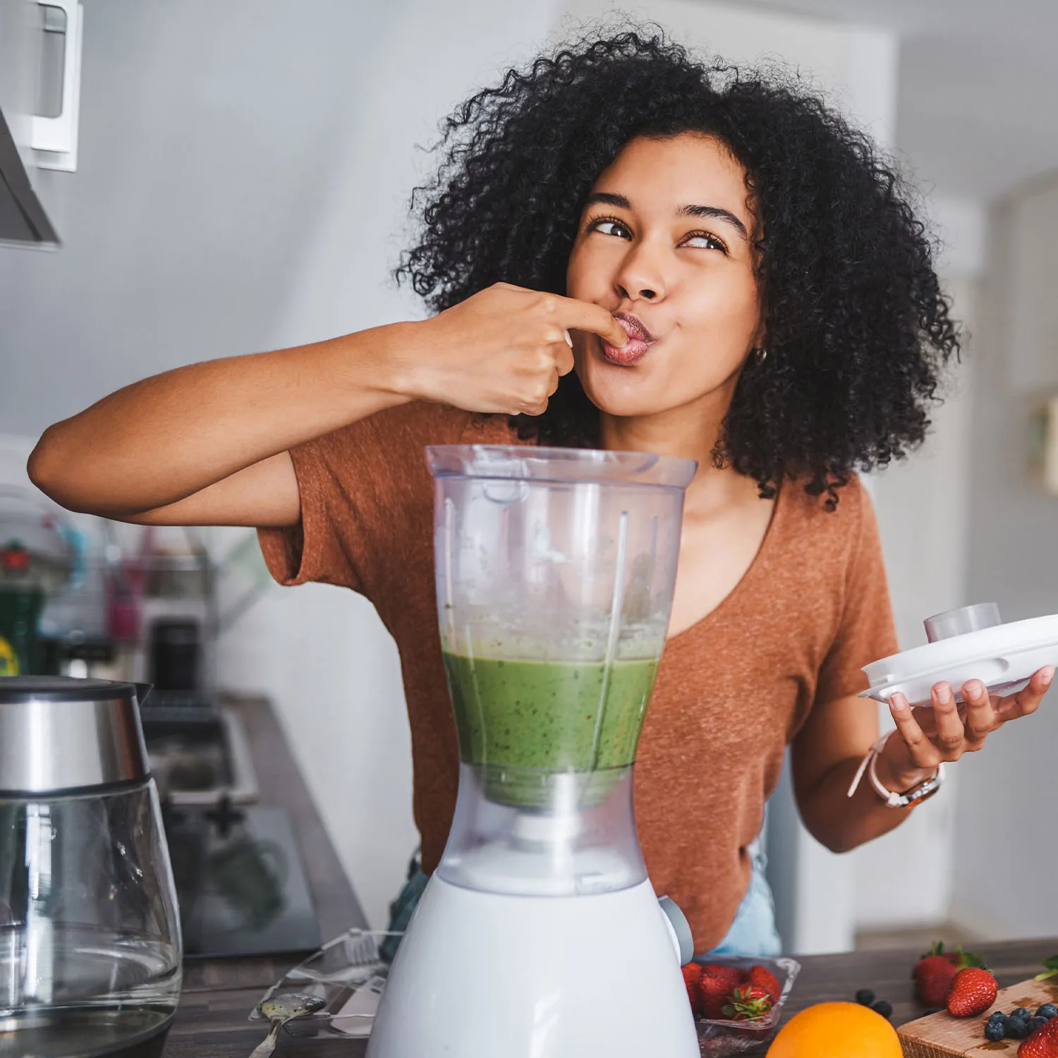 Eine Frau die einen gesunden Smoothie in einem Mixer mit einem Finger probiert.