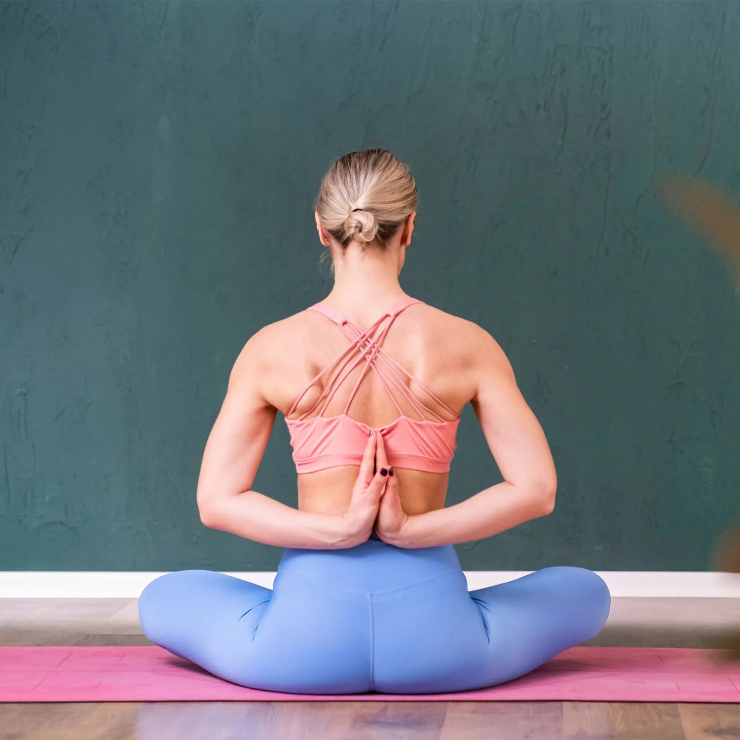 Eine Frau befindet sich in der Lotusposition und führt Yoga aus, wobei sie mit dem Rücken zur Kamera sitzt.
