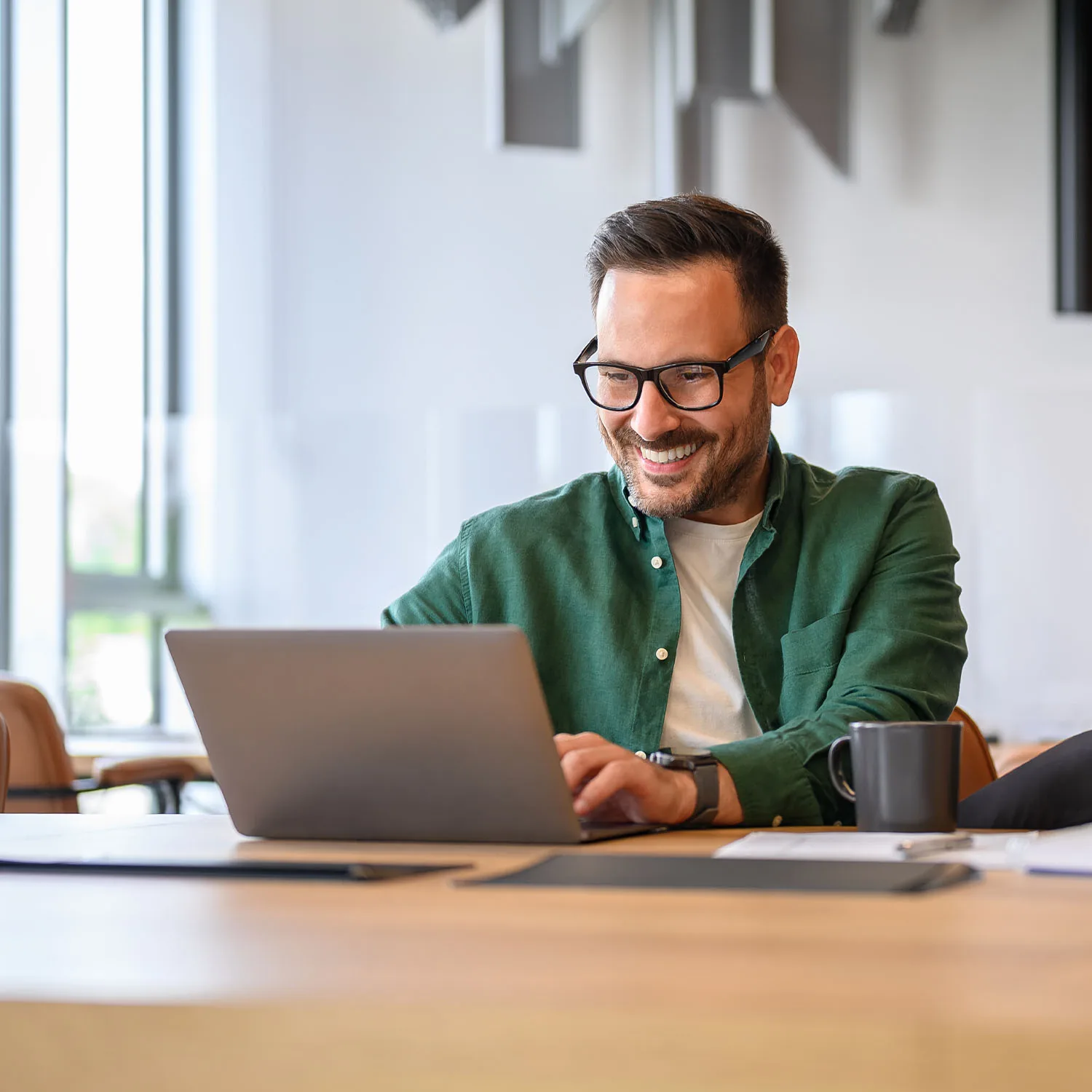 Ein Mann der glücklich lächelnd vor seinem Laptop sitzt.
