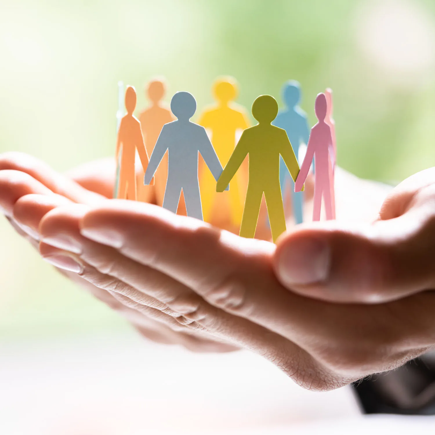 Zwei Hände hält einen Kreis aus bunten Papiermenschen, die sich an den Händen halten.