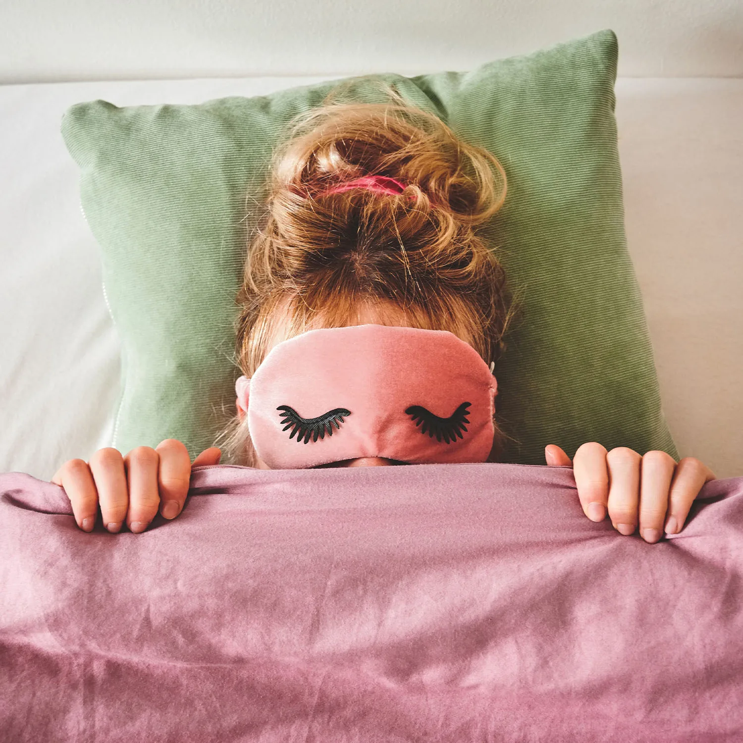 Eine Person trägt eine Schlafmaske und liegt schlafend in ihrem Bett.