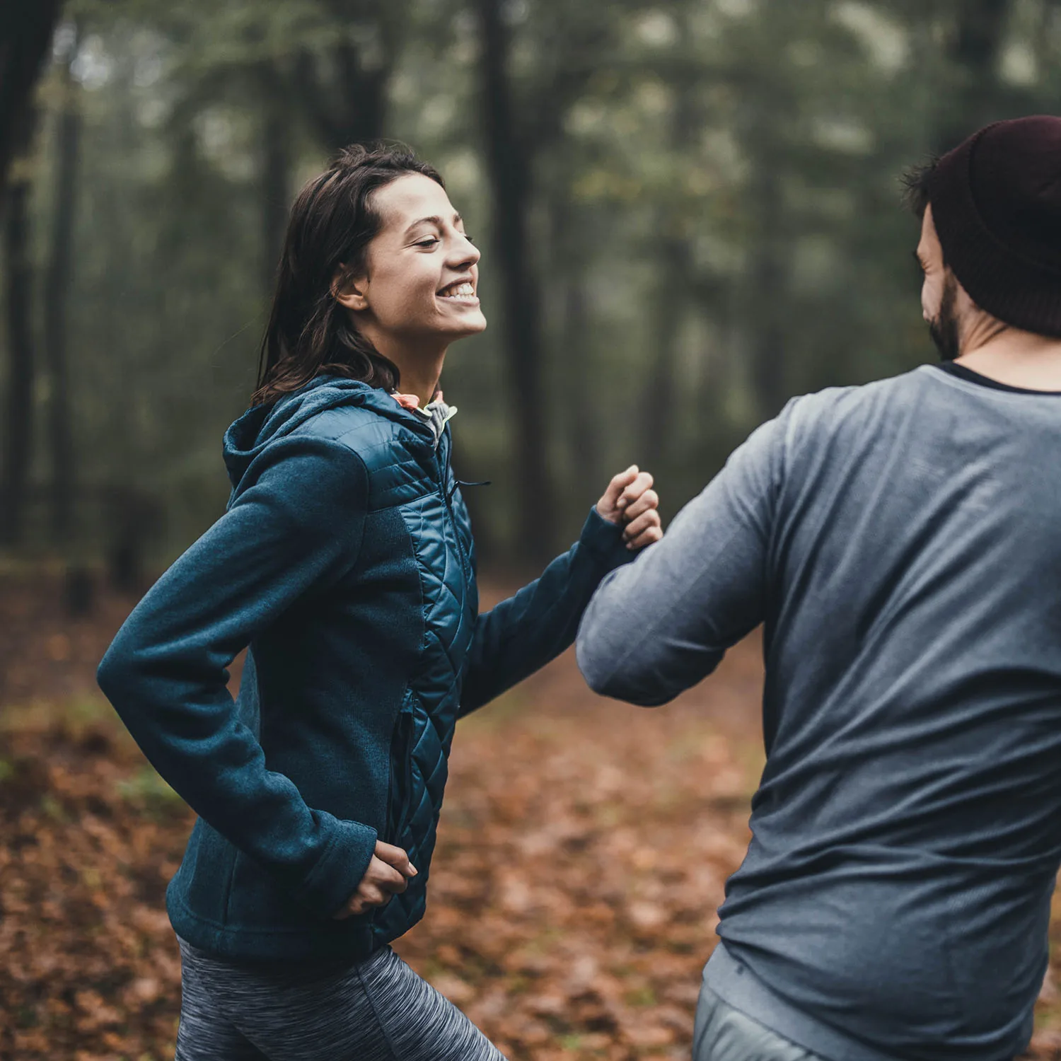 Zwei Personen die glücklich durch einen Wald joggen.