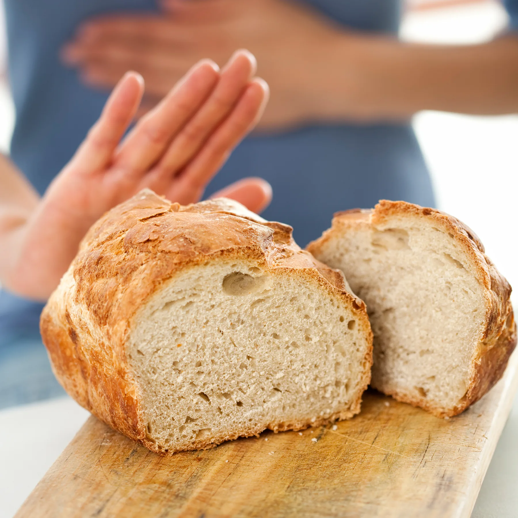 Eine Frau hält ihren Magen und macht eine Stop-Geste zu dem Weißbrot, was vor ihr liegt.